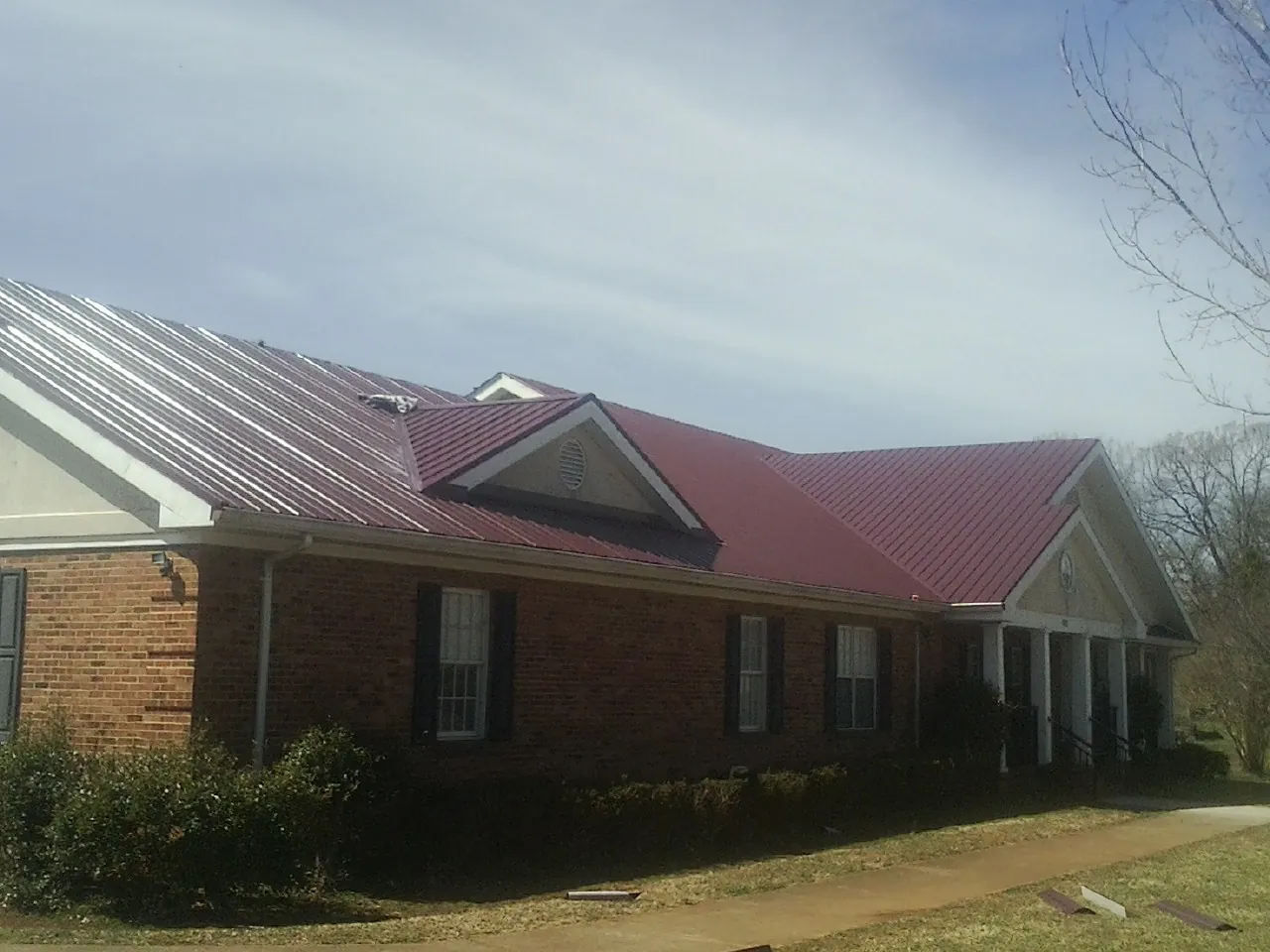 Red metal roof with gabled entries on a long brick building, from a Hail Damage Roof Repair job in Camilla