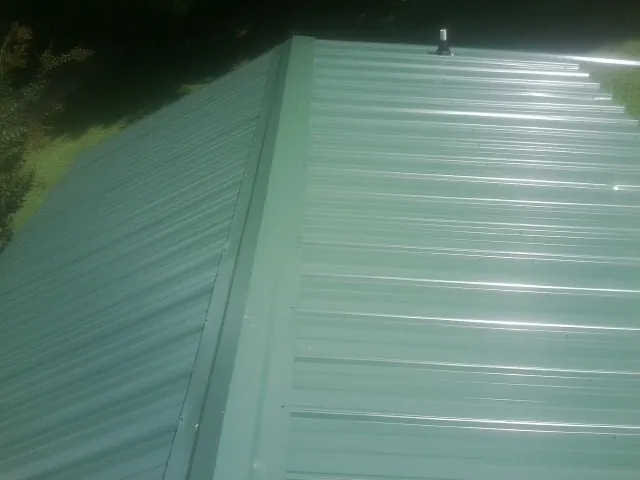 New green metal panels meeting at the ridge of a roof — Flat Roof Repair work by our crew in Camilla