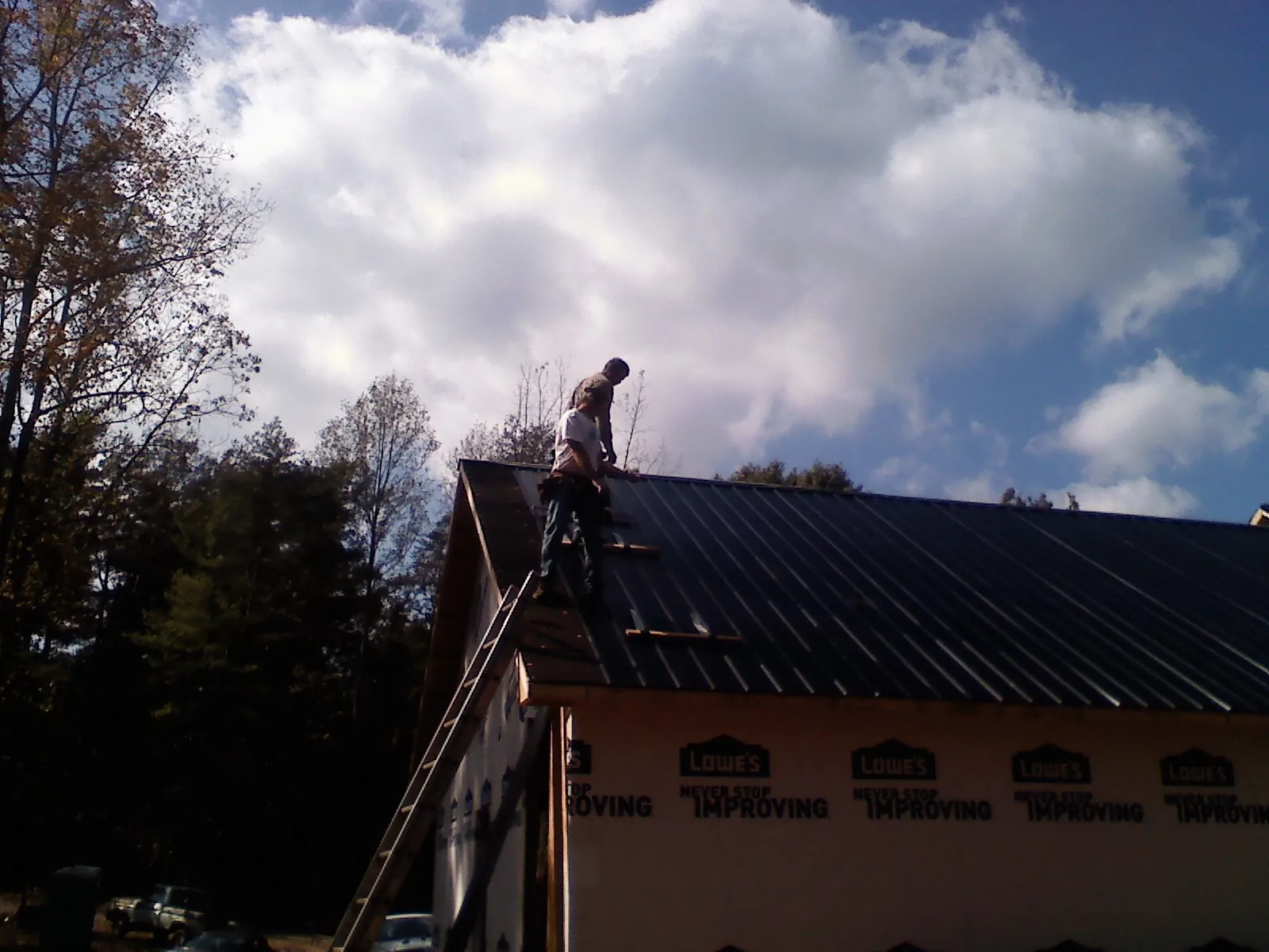 Roofer fastening dark metal panels high against a cloudy sky, from a Roof Inspection job in Camilla