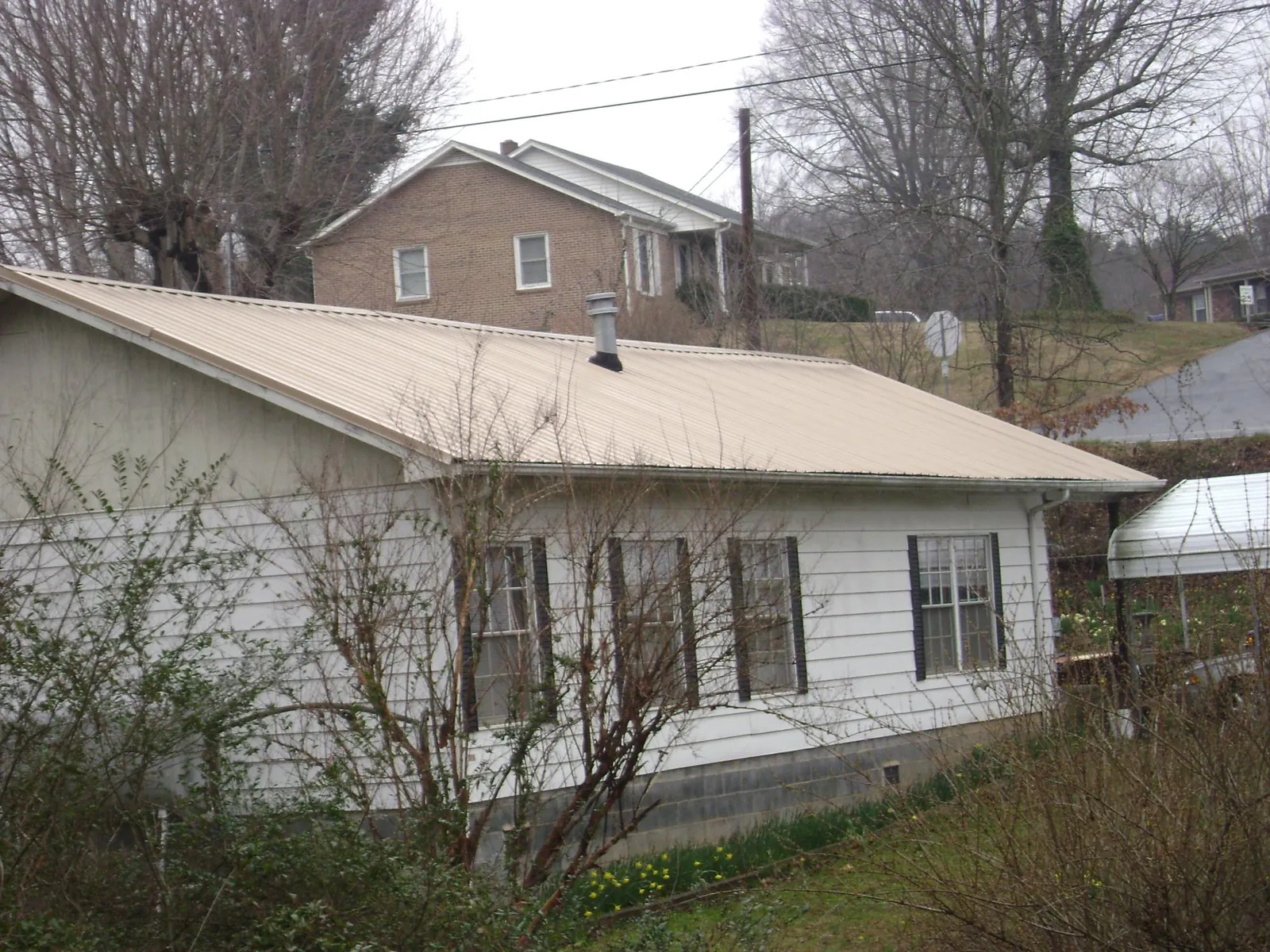 Tan metal roof on a white sided house set into a hillside — Commercial Roofing by Roofing Brothers in Camilla