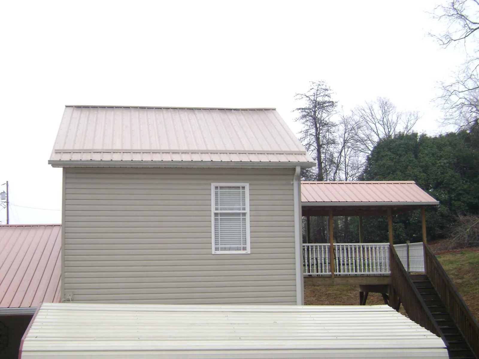 Tan metal roofs on a two story addition and attached porch, from a Roof Replacement job in Camilla